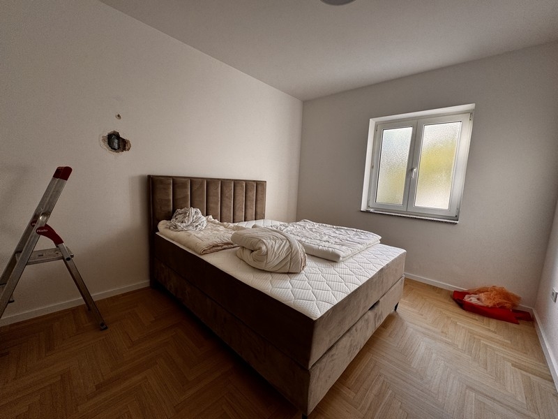 Ložnice s velkou čalouněnou postelí, bílými přikrývkami a malým oknem