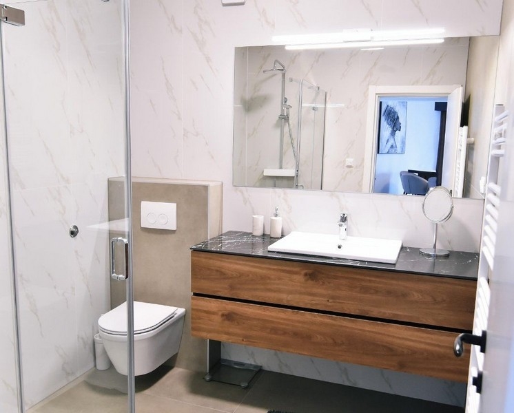 Moderní koupelna se sprchovým koutem, umyvadlem a dřevěnou komodou.