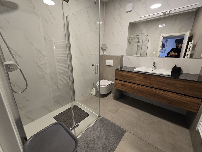 Prostorná koupelna se sprchovým koutem, umyvadlem a elegantními obklady.