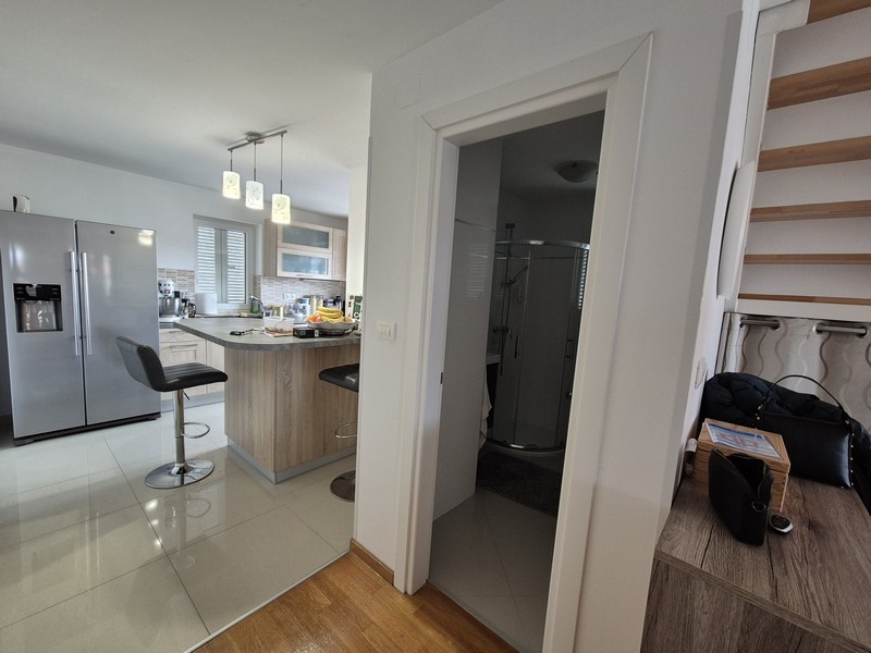 Otevřená kuchyně s ostrůvkem, barovými židlemi a vstupem do koupelny