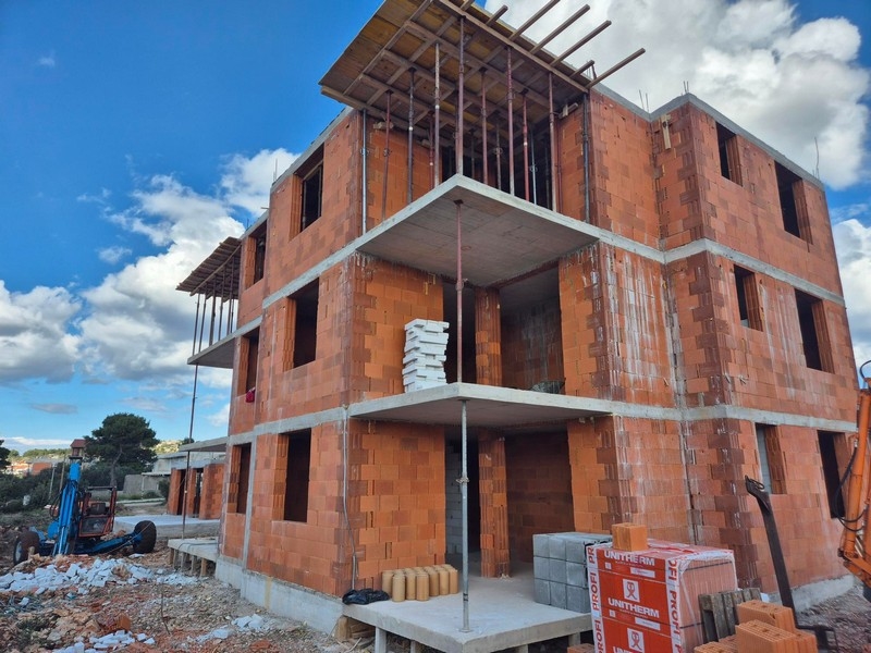 Novostavba třípodlažního bytového domu s otevřenými balkony a stavebními materiály