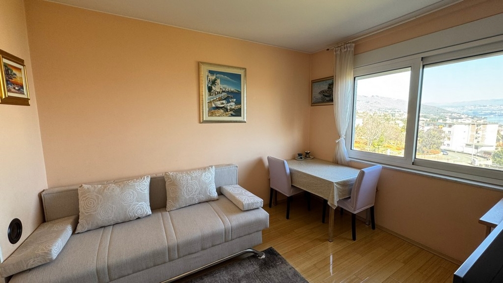 Obývací pokoj s pohovkou, stolem a velkým oknem s výhledem na moře