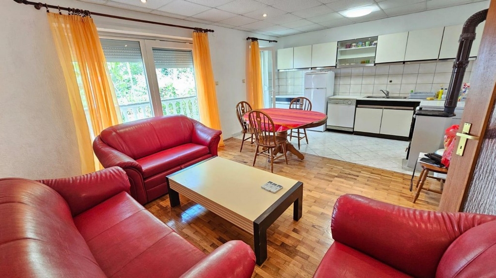 Obývací pokoj s červenou koženou pohovkou, přístupem na balkon a otevřenou kuchyní