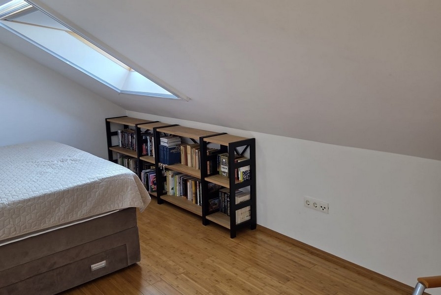 Ložnice se zkoseným stropem a policemi na knihy