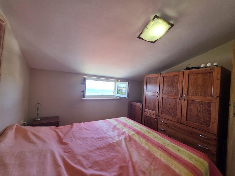 Ložnice s manželskou postelí a oknem s výhledem na moře.