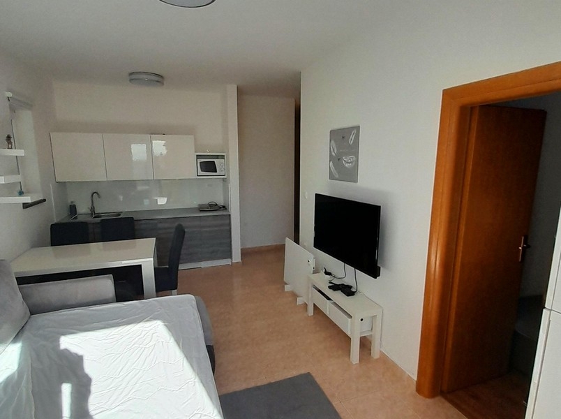 Obývací pokoj s televizí, jídelním stolem a vstupem do ložnice