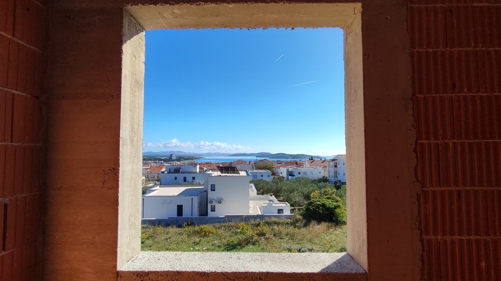 Pohled přes nedokončená okna na moře a obytnou zónu