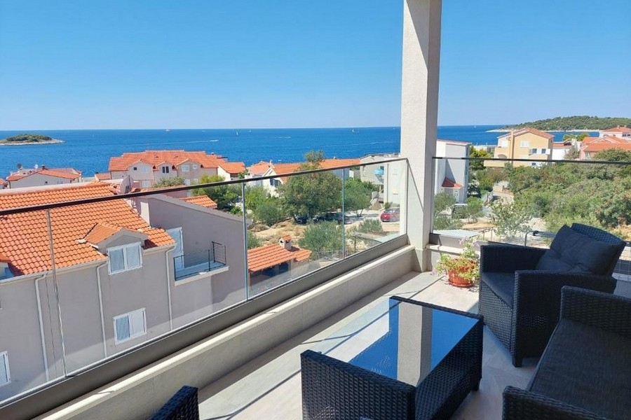 Krytý balkon s obývacím nábytkem a panoramatickým výhledem na moře