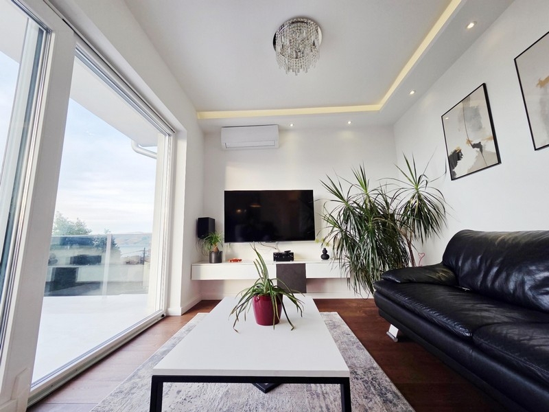 Obývací pokoj s velkým proskleným průčelím a vstupem na terasu s výhledem na moře