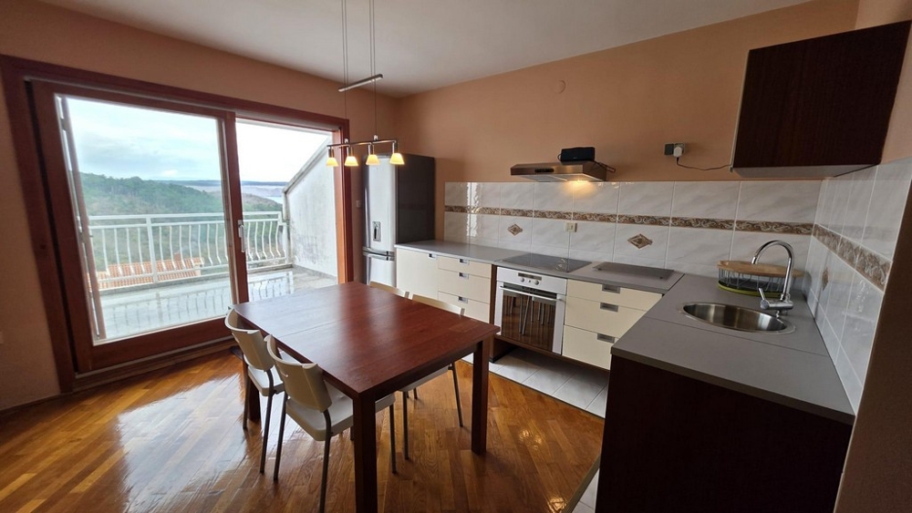 Obývací pokoj s integrovaným kuchyňským koutem a výhledem na terasu.