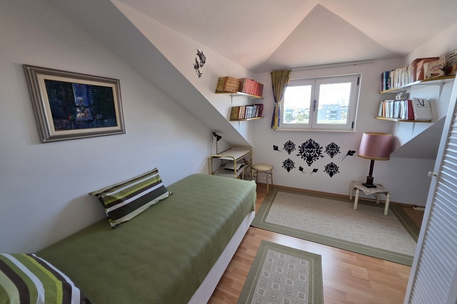 Světlá podkrovní ložnice se samostatným lůžkem, pracovním koutem a zkosenými stropy