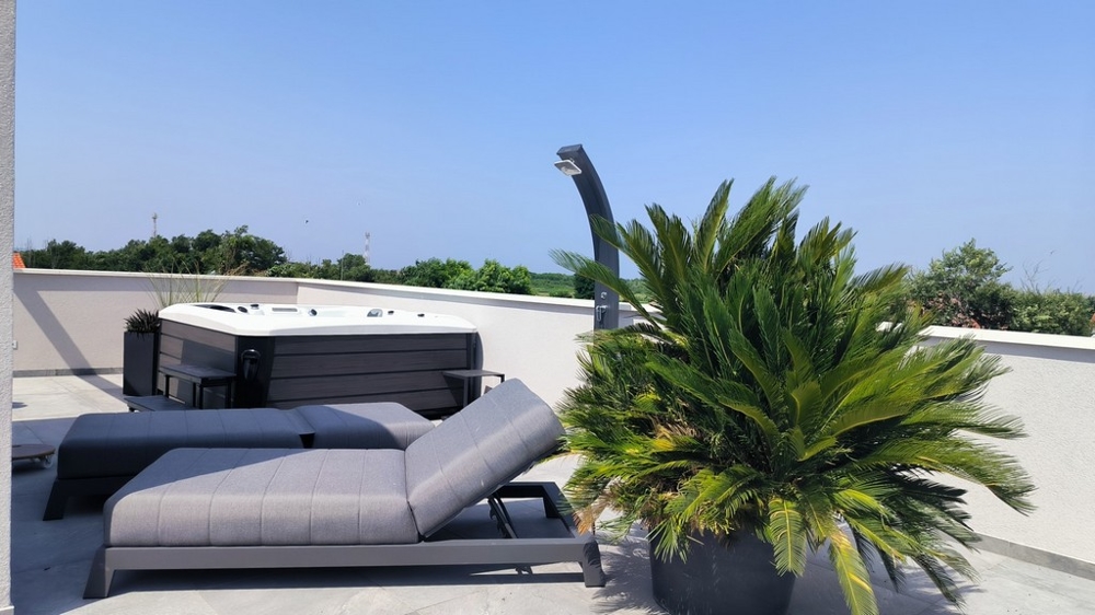 Střešní terasa s lehátkem, vířivkou a výhledem do krajiny.