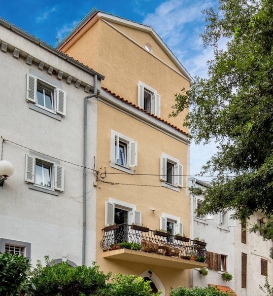 Fasáda žlutého domu jako součást nemovitosti v Chorvatsku s balkony a okenicemi