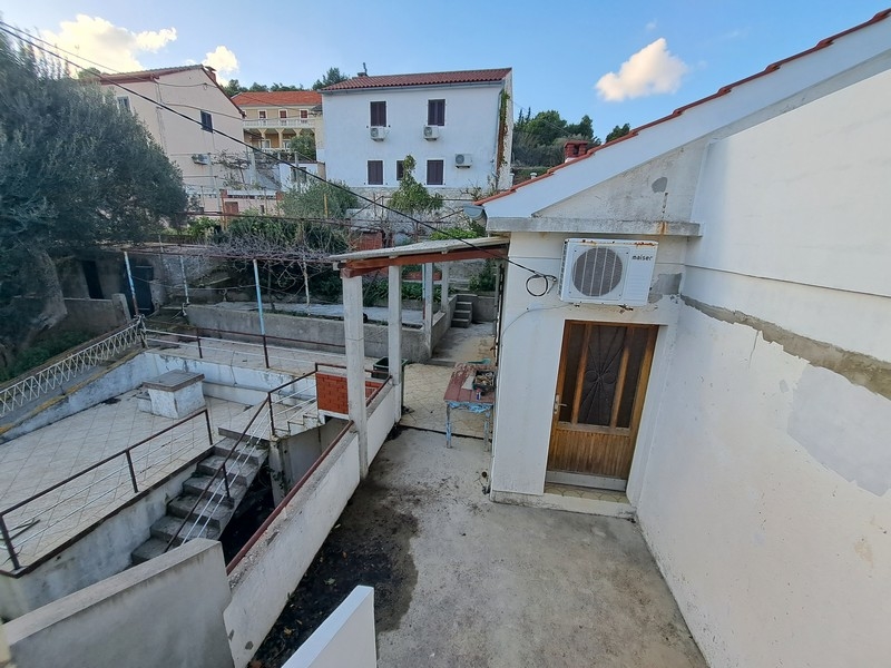 Dvorek chorvatského pozemku se zastřešenou terasou a schody, nabízený k prodeji společností Panorama Scouting.