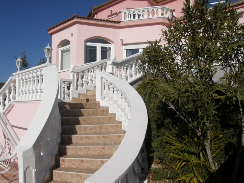 Čelní pohled na růžovou vilu v Chorvatsku s klikatými bílými schody a středomořskou vegetací