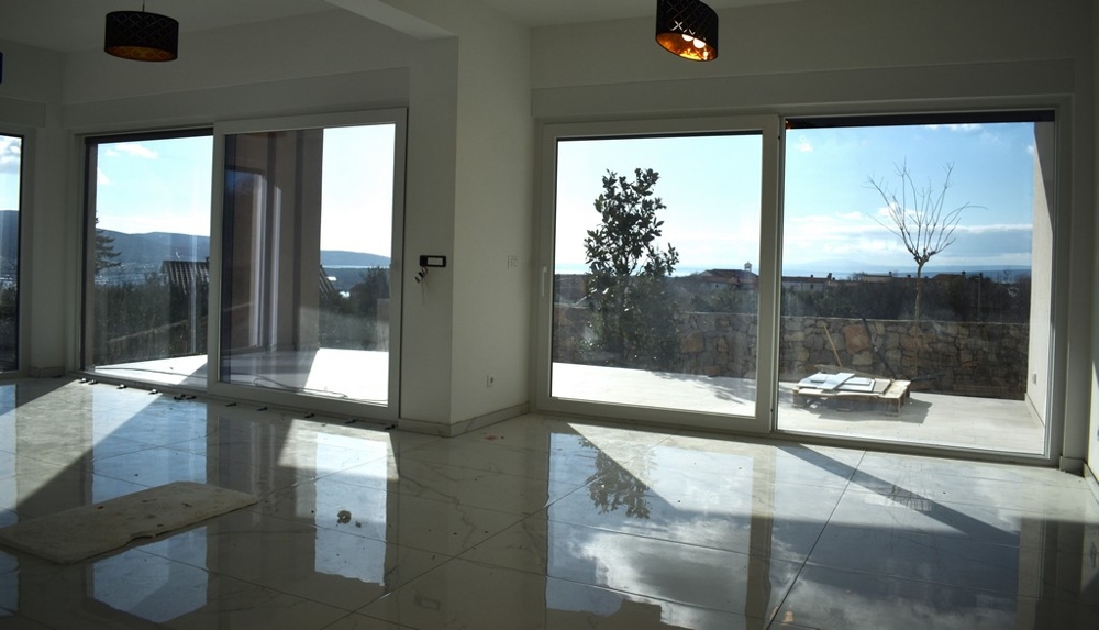 Prostorný, prázdný obývací pokoj s bílými stěnami a velkým oknem ve vile na Krku.