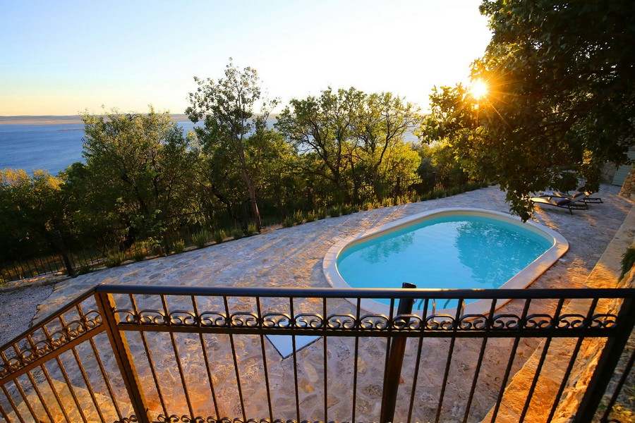 Bazén chorvatského kamenného domu na prodej, se západem slunce a výhledem na moře v pozadí.