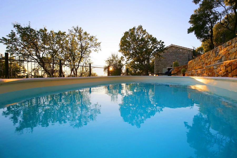 Bazén s čistou vodou ve venkovním areálu chorvatského kamenného domu na prodej, s odrazem oblohy.