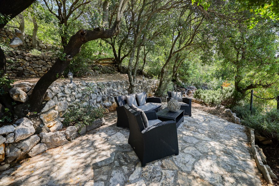 Venkovní salonek kamenného domu na prodej v Chorvatsku, obklopený stromy a přírodními kamennými zdmi.