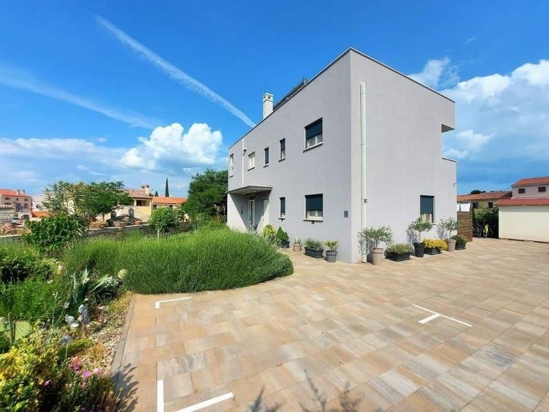 Čelní pohled na moderní tříbytový dům na prodej na Istrii, s dlážděným nádvořím a obklopeným rostlinami v květináčích.