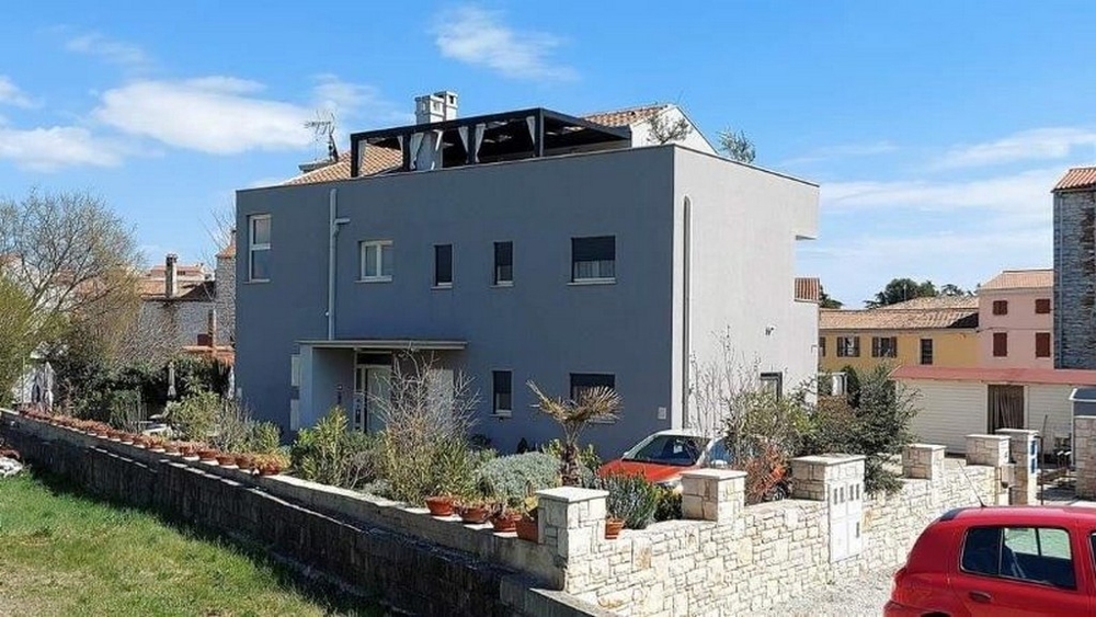 Boční pohled na tříbytový dům na prodej na Istrii, s terasou a rostlinnou výzdobou podél plotu.