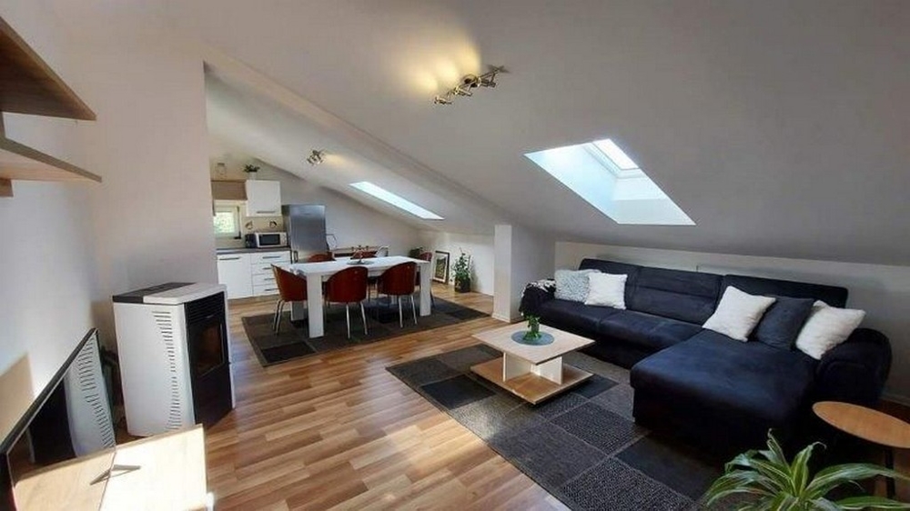 Útulný obývací pokoj v podkroví domu se třemi byty na Istrii, na prodej, s pohovkou, jídelním stolem a otevřeným kuchyňským koutem.