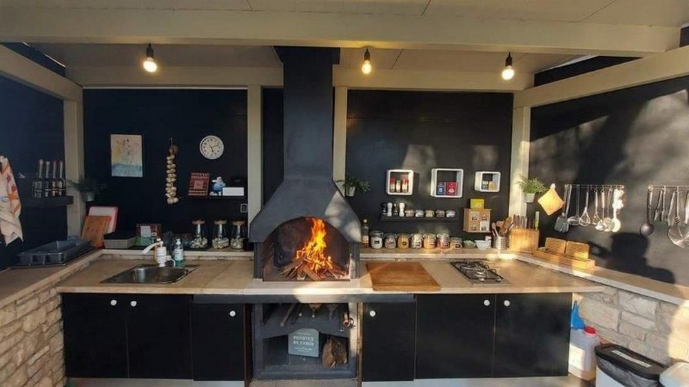 Kuchyně s krbem na grilování v domě se třemi byty na Istrii, na prodej, s černými pracovními plochami a moderními kuchyňskými spotřebiči.