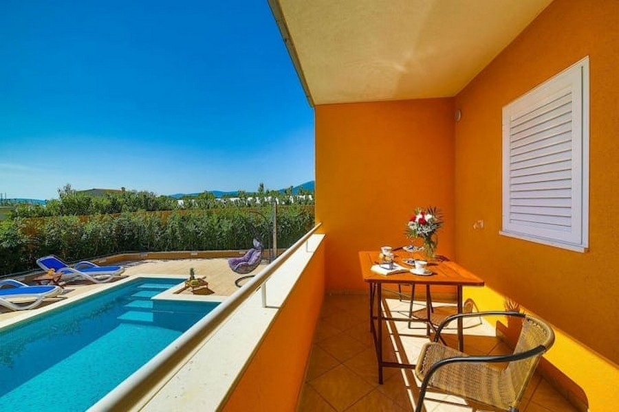 Pohled z balkonu na bazén v apartmánovém domě v Kaštel Lukšić, Chorvatsko, se stolem a židlemi