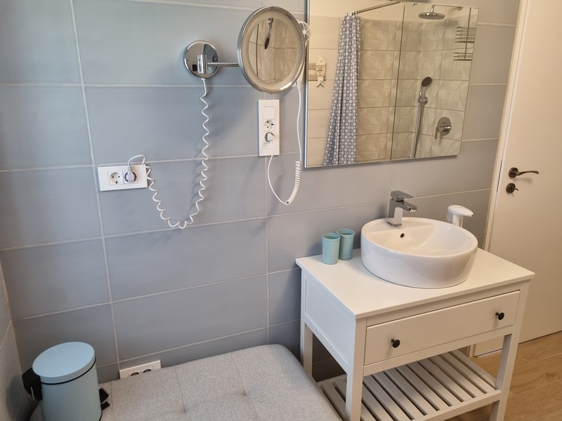 Koupelna v přímořském činžovním domě na prodej v Karlobagu, Chorvatsko, se světle modrými dlaždicemi, bílou konzolou, zrcadlem a věšákem na ručníky