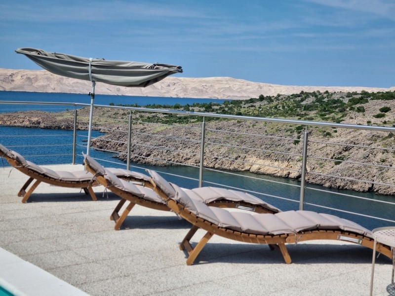 Relaxační zóna s lehátky a slunečníkem na terase činžovního domu v Karlobagu, Chorvatsko, s výhledem na moře.