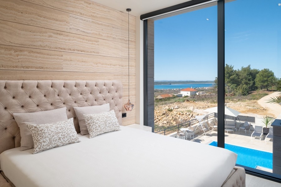 Elegantní ložnice ve vile na prodej v Ražanac, Zadar, Chorvatsko, s velkou postelí a čelem, výhledem na moře a přístupem k bazénu.