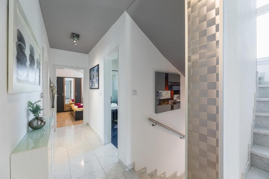 Vstupní prostor a chodba bytového domu v Chorvatsku s výhledem na moře, s lesklými dlaždicemi, schodištěm a nástěnnými dekoracemi