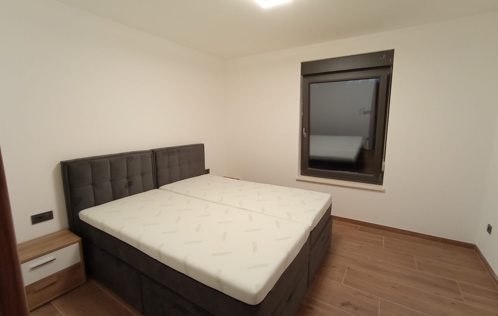 Podobná perspektiva ložnice nemovitosti v Chorvatsku, s nočním stolkem a zavřeným oknem.