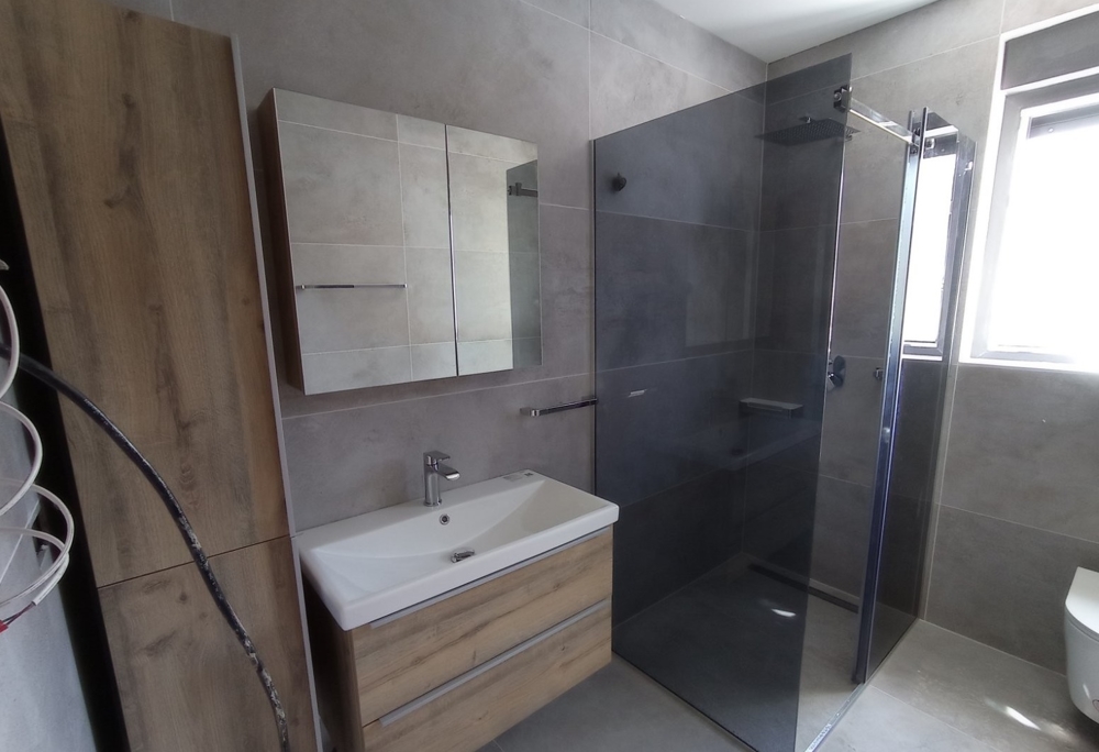 Moderní koupelna se sprchovým koutem v nemovitosti v Chorvatsku, zrcadlová skříňka a dřevěné prvky v designu.