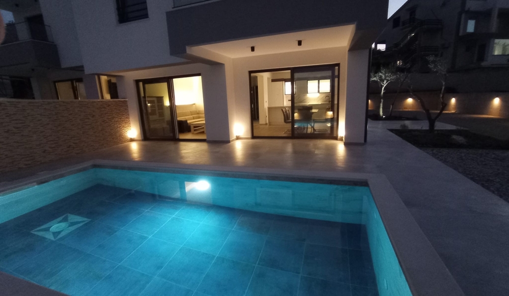 Soumrakový výhled na terasu a bazén nemovitosti v Chorvatsku, vnitřní osvětlení vytváří příjemnou atmosféru.