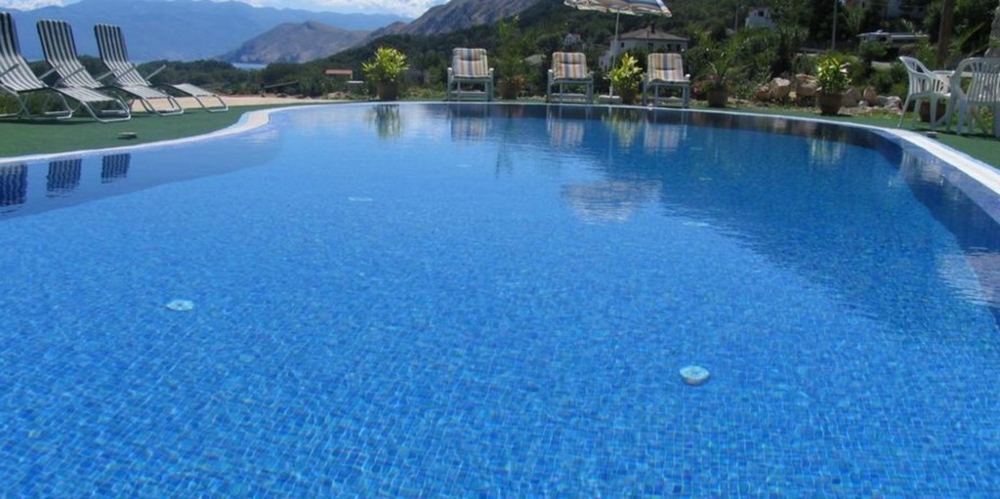 Modrý bazén s výhledem na hory obklopený lehátky, chorvatské nemovitosti