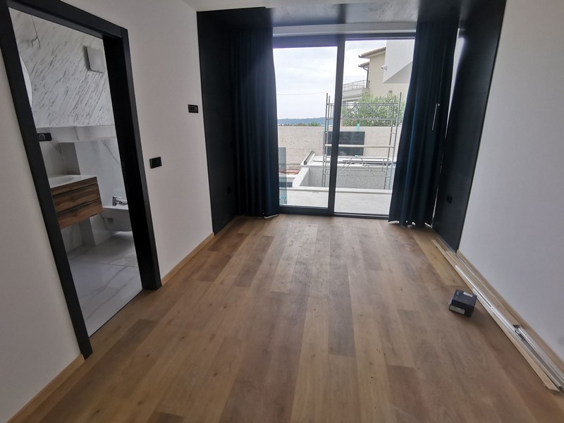 Vnitřní pohled na ložnici s dřevěnými podlahami a velkým oknem