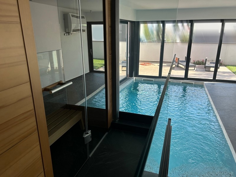 Vnitřní bazén vily s prosklenými stěnami spojující bazénovou část se zahradou