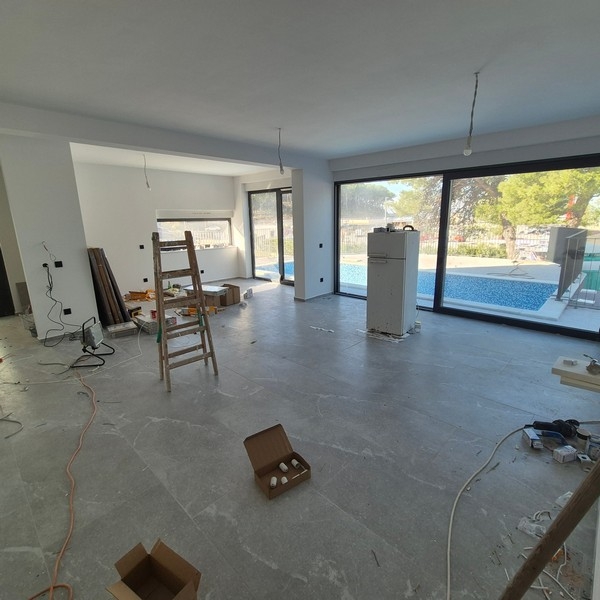 Moderní dvoupatrová vila s velkými okny, balkony a dvougaráží, s elegantním vozem vpředu, se nachází v Drage, Chorvatsko.