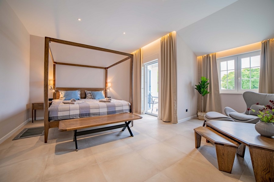 Prostorná ložnice s postelí s nebesy, lavicí a pohodlným sezením, zařízená ve světlých barvách a se spoustou přirozeného světla