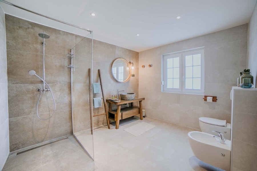 Luxusní koupelna s velkým sprchovým koutem, bidetem a rustikálním dřevěným umyvadlem, navržená v zemitých tónech a moderním vybavením