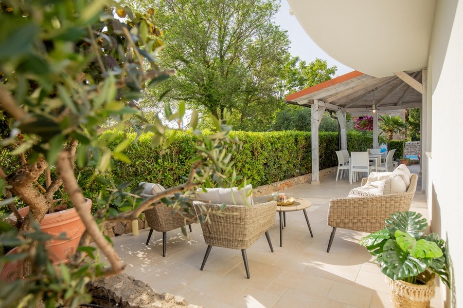 Venkovní posezení s proutěným nábytkem a stinným jídelním koutem obklopeným zelení a stromy