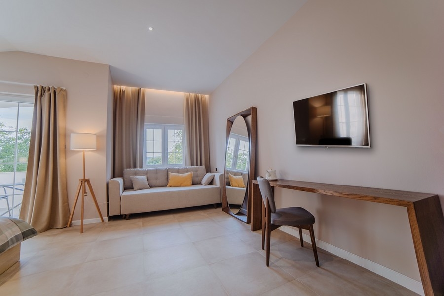 Útulný obývací pokoj s několika pohovkami, TV a velkými okny s modrými závěsy, které propouštějí přirozené světlo