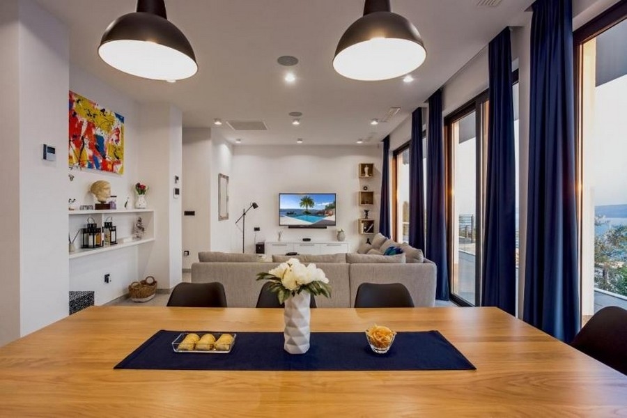 Obývací pokoj s velkou pohovkou, TV s plochou obrazovkou a výhledem na moře přes velká okna