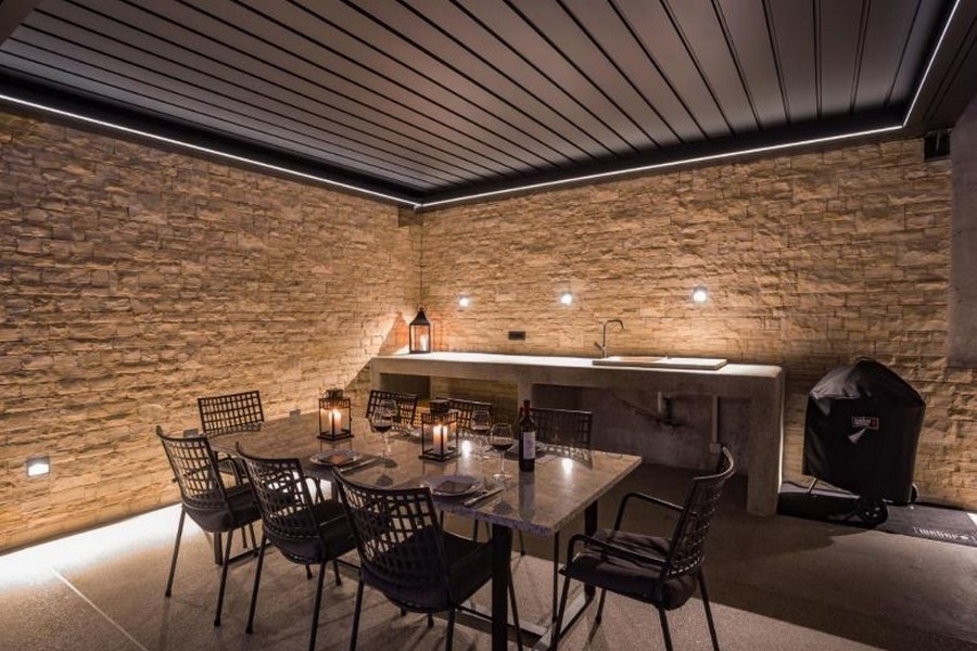 Krytý venkovní prostor s jídelním koutem a grilem, obklopený kamennými zdmi