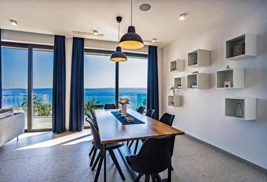 Jídelna s moderním dřevěným stolem, černými židlemi a panoramatickým výhledem na moře