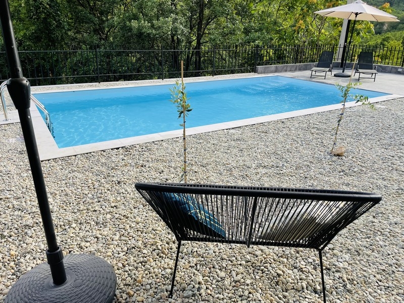 Bazén v zahradě, obklopený oblázky, s výhledem na les