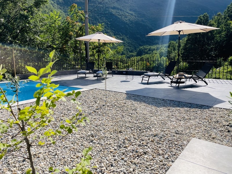 Sluneční terasa u bazénu s lehátky a slunečníky, obklopená zelení