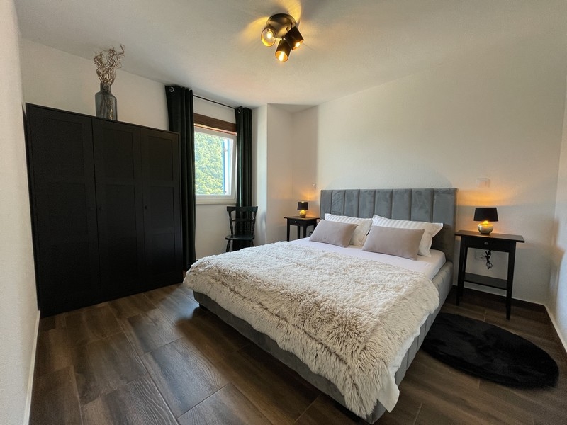 Ložnice s šedou postelí, černou skříní a dvěma nočními stolky osvětlenými teplým světlem