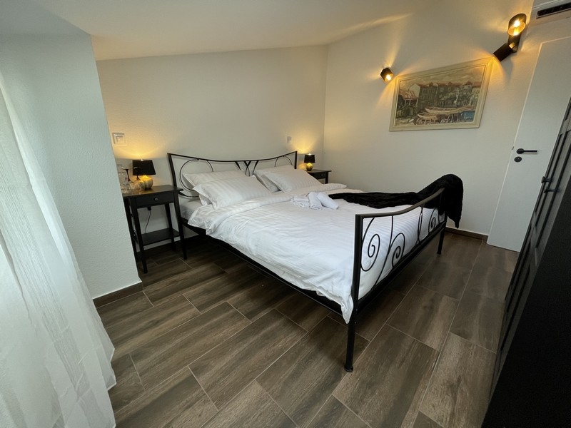 Ložnice s kovanou postelí, dřevěnými podlahovými a nástěnnými svítidly, s bočním výhledem na obraz